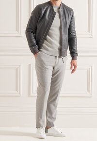 Giacca bomber in pelle grigio scuro, maglione grigio sotto, pantaloni tapered grigio chiaro e sneakers bianche con un accento verde.