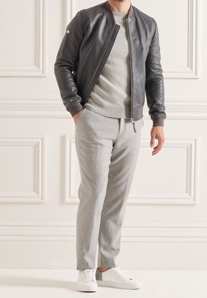 Giacca bomber in pelle grigio scuro, maglione grigio sotto, pantaloni tapered grigio chiaro e sneakers bianche con un accento verde.