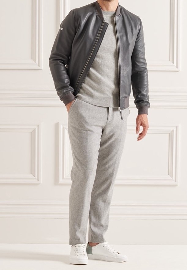 Giacca bomber in pelle grigio scuro, maglione grigio sotto, pantaloni tapered grigio chiaro e sneakers bianche con un accento verde.