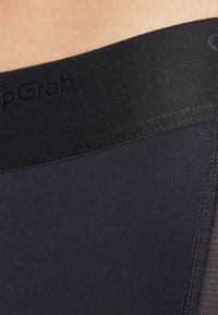 Schwarze Kompressionsshorts mit breitem elastischem Bund, der ein geprägtes Logo aufweist. Glattes, mattes Material mit verstärkten Nähten an der Seite.