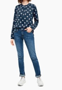 Navy long-sleeve blouse with white circular patterns, paired with fitted blue jeans and white sneakers. Blouse features a pleated neckline.