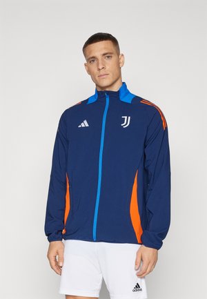 Chaqueta de marina con toques en naranja y azul, cierre completo en la parte delantera, cuello alto y bolsillos laterales. Presenta los logos de adidas y Juventus. Material ligero.