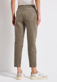 Pantalons en coton kaki à coupe décontractée, avec une taille élastique et deux poches arrière. Portés avec des baskets blanches et beiges.
