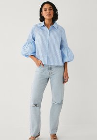 Lyseblå stribet bluse med puffede ærmer og knaplukning. Kombinationen med lyseblå slidte jeans og beige sandaler.