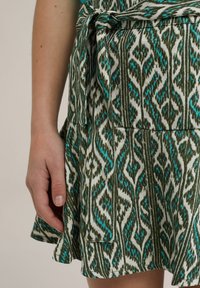 Green and white patterned dress featuring an abstract print, a tied waist, and a flared hem; made from a lightweight fabric.