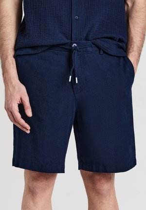 Shorts bleu marine en tissu doux, dotés d'une taille avec cordon de serrage, de poches latérales et d'une coupe décontractée avec un ourlet droit.