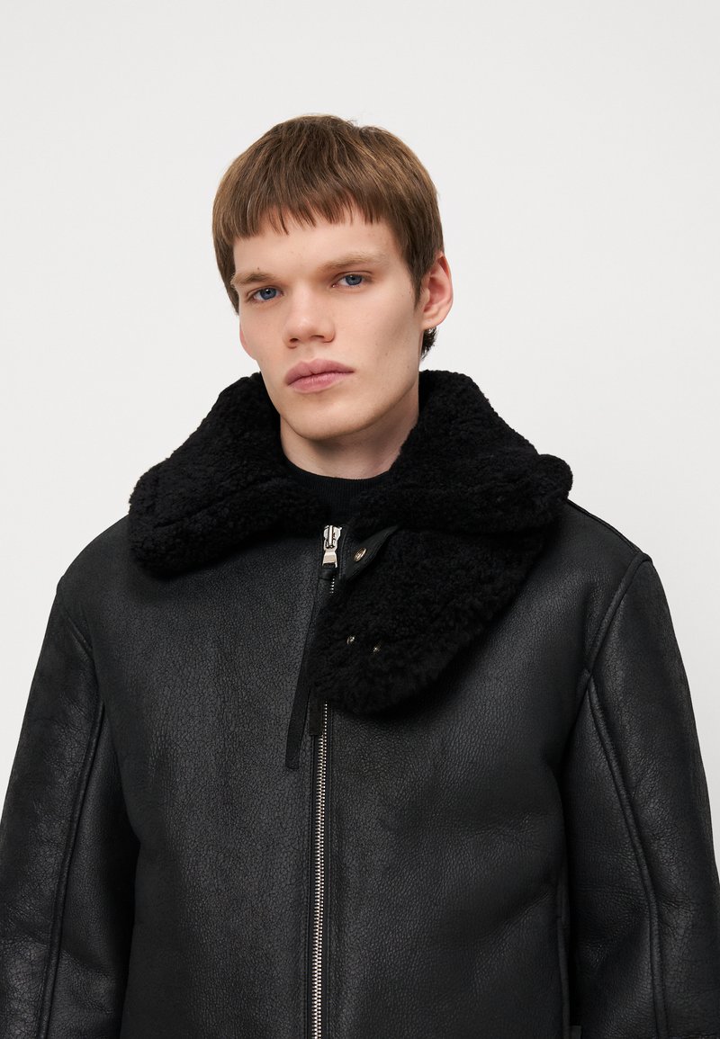 Chaqueta de cuero negra con un suave collar negro, que presenta un cierre frontal y un acabado texturizado. Diseño sencillo sin patrones ni acentos visibles.