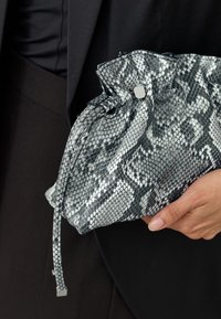 Sac pochette à motif peau de serpent noir et blanc avec un design plissé, une fermeture à cordon de serrage et un détail métallique. Surface texturée visible.