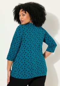 Türkise Bluse mit schwarzem kreisförmigem Muster, dreiviertellangen Ärmeln, abgerundetem Saum und glatter Textur, mit lässiger Passform und schlichter Ausschnitt.