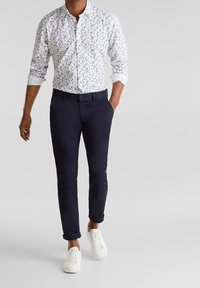 Chemise blanche boutonnée avec un motif floral, pantalon slim marine, et baskets blanches, créant un look décontracté et coordonné.
