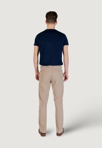 T-shirt a maniche corte blu navy abbinato a pantaloni beige. I pantaloni hanno un taglio dritto, due tasche posteriori e sono indossati con scarpe marroni.