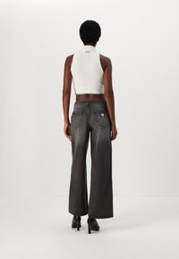 Balta bez piedurknēm adīta blūze apvienota ar augstām, platām melnām džinsām, kuru sānos ir neliela logo birka un aizmugurējās kabatas. Melnie zābaki noslēdz izskatu.