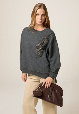Sweat-shirt gris avec un design floral embelli sur le devant, associé à un pantalon beige et un sac à main en cuir brun avec une chaîne.