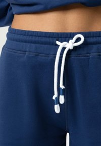Marineblauwe joggingbroek met een taillekoord met witte veters en tweekleurige accenten. Gemaakt van zacht stof met een gladde textuur.