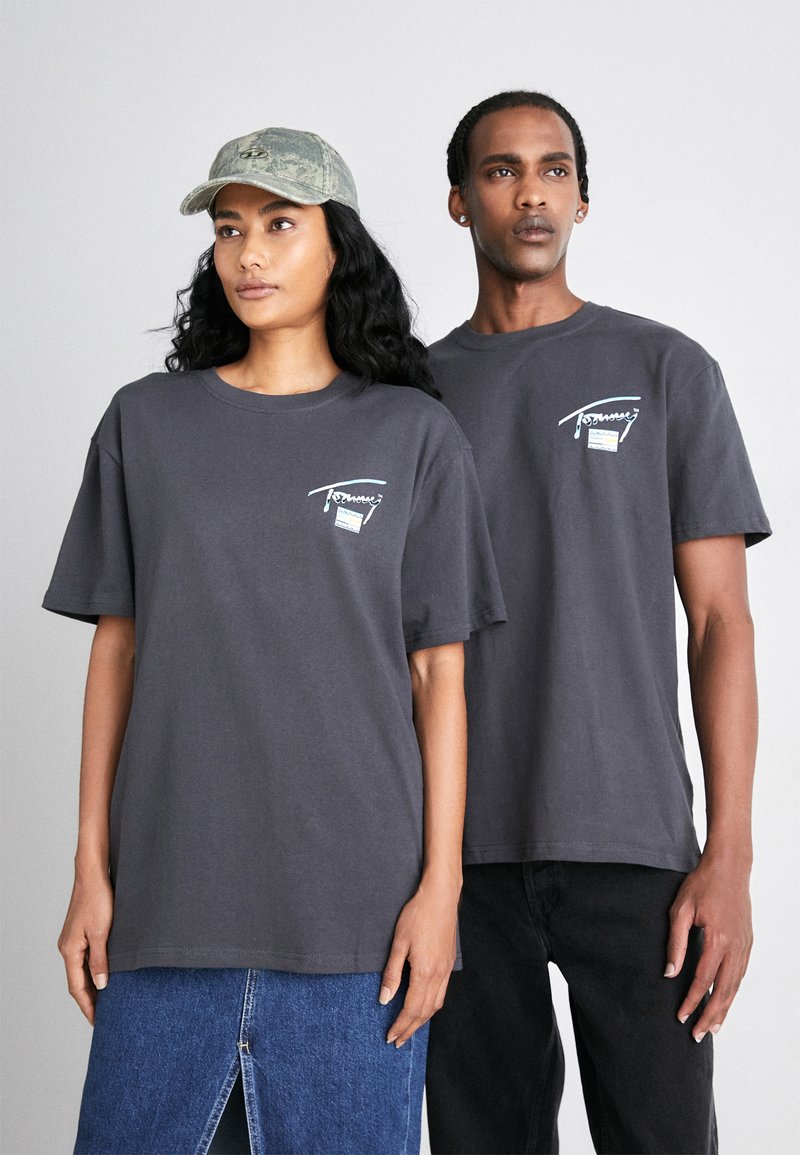 Camisetas de algodón gris usadas por dos personas, con un pequeño gráfico en la parte frontal y mangas cortas. Una persona lleva una gorra de camuflaje.
