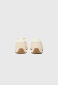 Sneakers with a creamy upper featuring a mix of textures; soft suede heel counter, rubber sole with a wavy pattern, and light color scheme.