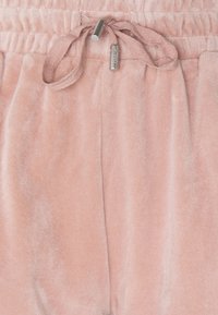 Joggers en velours rose clair avec une taille élastique et un cordon de serrage assorti, présentant une texture légèrement brillante. Tissu doux et confortable.