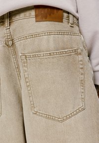 Behke denim-housut, joissa on lievästi haalistunut pinta. Takana on tasku ja nahkalaikku, jossa on kohokuvioitu logo. Säädettävä vyötäröpehmuste.