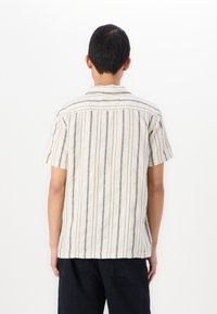 Camicia a maniche corte in tessuto crema con strisce verticali blu navy. Presenta un colletto classico e una superficie leggermente texturizzata.