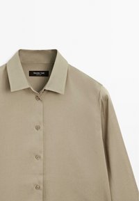 Camicia beige con colletto classico, realizzata in tessuto liscio. Presenta cinque bottoni sul davanti e una leggera lucentezza.