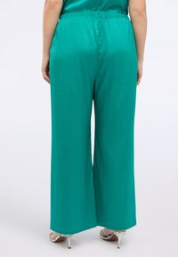 Kalhoty s širokým střihem vyrobené z hladké, tyrkysové látky. Mají elastický pas a decentní geometrickou texturu.