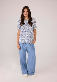 Helles, blaues Oberteil mit Blumenmuster und kurzen Ärmeln, kombiniert mit weit geschnittenen, hellblauen Jeans und weißen Schuhen.