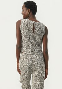 Ærmeløs jumpsuit med et brunt og hvidt abstrakt mønster, med en nøglehulslukning bagpå og elastisk talje for komfort.