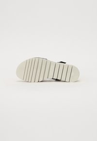 Sandale noire avec une semelle en caoutchouc texturée de couleur blanc cassé. Présente des rainures horizontales épaisses pour une meilleure adhérence. Design minimaliste sans marquage visible.