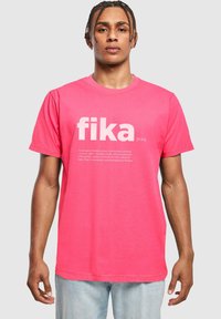 Camiseta de algodón rosa con el gran texto blanco "fika" y una definición debajo. La camiseta tiene mangas cortas y un corte clásico.