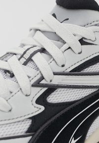 Baskets blanches et noires en matériaux mesh et synthétiques, avec des lacets plats, des coutures délicates et une surface texturée.