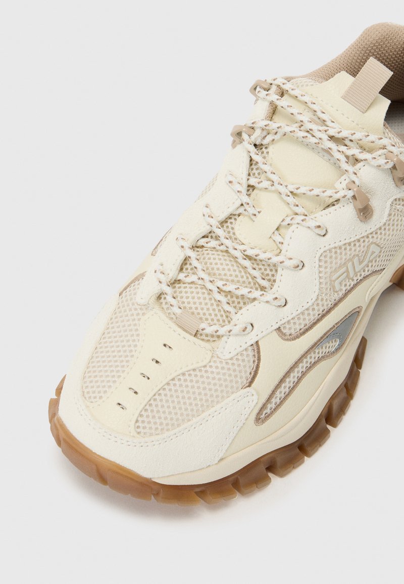 Cremfarbene und beige Sport Schuh mit Mesh-Einsätzen, strukturierten Überzügen, Schnürsenkeln mit reflektierenden Details und einer Gummisohle mit einem Wabenmuster.