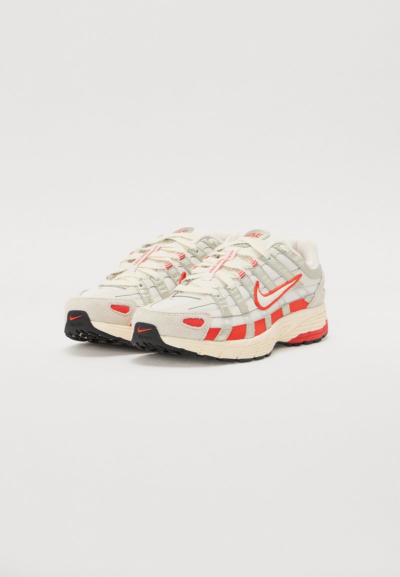Nike Sneaker in Beige mit roten Akzenten, ausgestattet mit einem Mesh-Obermaterial, strukturierten Überzügen und einer gemusterten Sohle für besseren Halt. Die Schnürsenkel sind elfenbeinfarben.