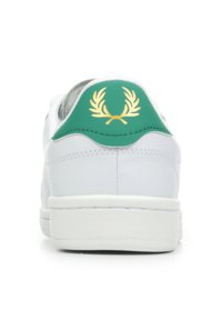 Zapatilla blanca con una pestaña verde en el talón que presenta un diseño de laurel dorado. Parte superior de cuero liso y suela de goma blanca. Diseño minimalista.