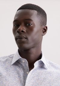 Camicia button-up con un motivo floreale azzurro chiaro, colletto e dettagli con bottoni. Il tessuto appare liscio con una fine trama.