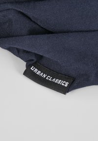 Jūros mėlynos spalvos audinys su lygiu paviršiumi, kampu featuring juodu etiketę su balta užrašu "URBAN CLASSICS".