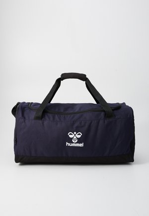 Σκούρο μπλε και μαύρη αθλητική τσάντα duffel με μαύρους χειρολαβές και λευκό λογότυπο "hummel" μπροστά, όρθια σε ένα απλό φόντο.