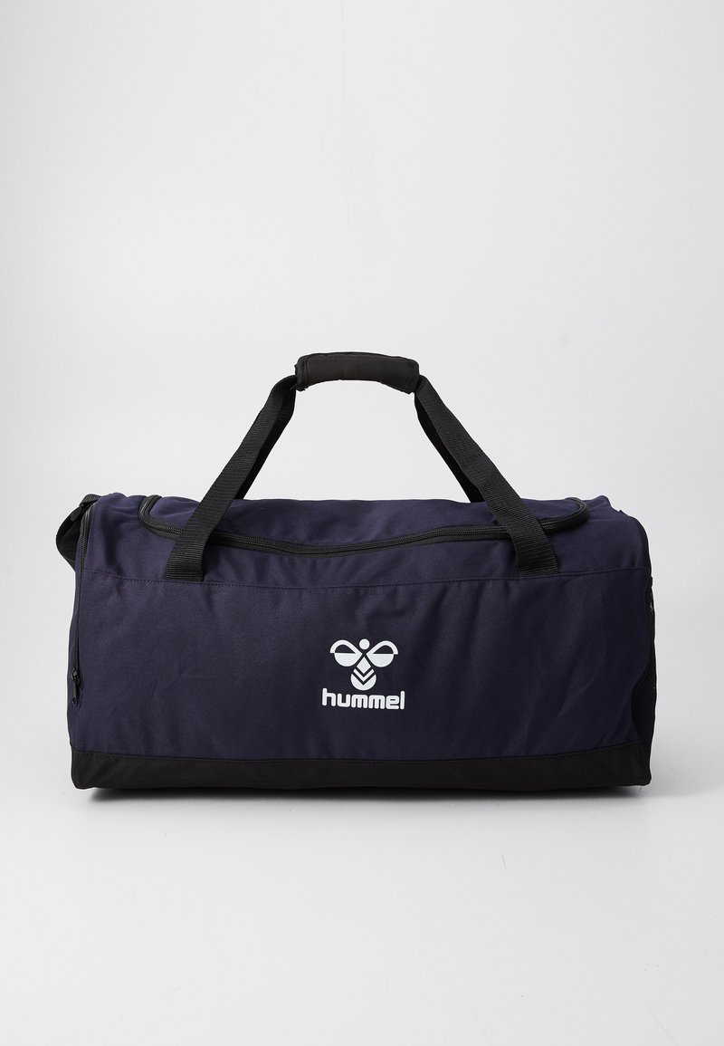 Tummansininen ja musta urheiluduffelilaukku, jossa mustat kahvat ja valkoinen "hummel"-logo edessä, seisoo pystyasennossa yksinkertaista taustaa vasten.