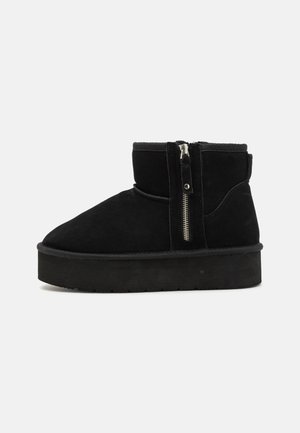 Fekete velúr bokacsizmák lapos talppal, oldalsó cipzárral és puha, texturált gallérral. Rövid, kerek orrú kialakítás.