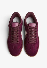Baskets en daim bourgogne avec lacets assortis, bandes blanches sur les côtés et semelle en caoutchouc marron contrastante. Tige texturée avec un col rembourré.