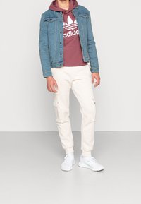 Jeansjacka, vinröd huppetröja med vit logotyp, cremefärgade cargobyxor med sidorfickor och vita träningsskor.