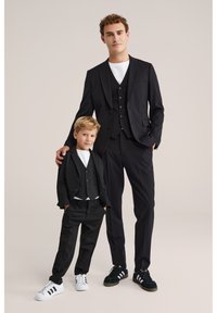 Černý oblek pro dospělé a dítě s úzkým střihem, tříknoflíkovými vestami, bílými tričky pod nimi a sladěnými teniskami.