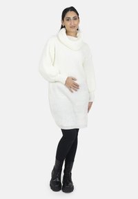 Witte gebreide sweaterjurk met een kolkraag en geribbelde textuur, gecombineerd met zwarte legging en zware zwarte veterlaarzen.