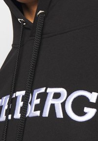 Sudadera negra con una gran bordado en blanco de la palabra "ICEBERG". Cuerdas ajustables con extremos metálicos y textura suave.