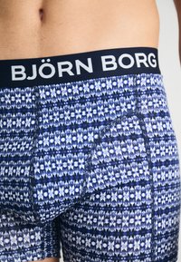 Moške bokserice z modro in belo geometrijsko sestavo, z črnim pasom z logotipom "BJÖRN BORG" in raztegljivim materialom.