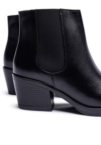 Botines negros de cuero con paneles laterales elásticos, tacones de bloque cónicos y textura suave. Presentan un diseño elegante y detalles mínimos.