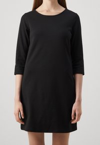 Robe en coton noire avec un col rond et des manches trois-quarts, présentant un design simple et droit ainsi qu'une texture douce.