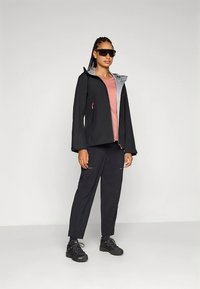 Zwarte waterdichte jas met een grijze capuchon, gecombineerd met een roze top en zwarte broek. Effen kleur ontwerp, minimale hardware en zakken met ritsen.