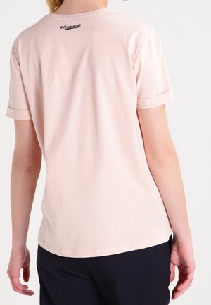 Person wearing a light pink short-sleeve shirt with "#TeamKarl" printed near the neckline on the back, paired with black pants.