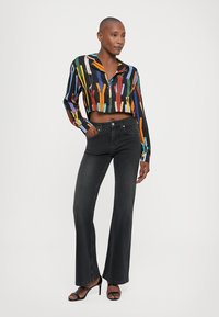 Blusa cropped con righe verticali multicolori e colletto, abbinata a jeans neri a zampa d'elefante e sandali neri con tacco. Texture liscia.