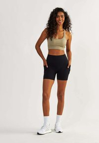 Light beige sports bra and black bike shorts with pockets. The outfit features a fitted design. Model wears white athletic shoes and socks.